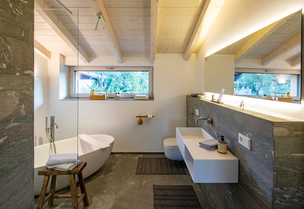 Immagine di una stanza da bagno padronale design con vasca freestanding, pareti bianche, lavabo sospeso, pavimento grigio e top bianco