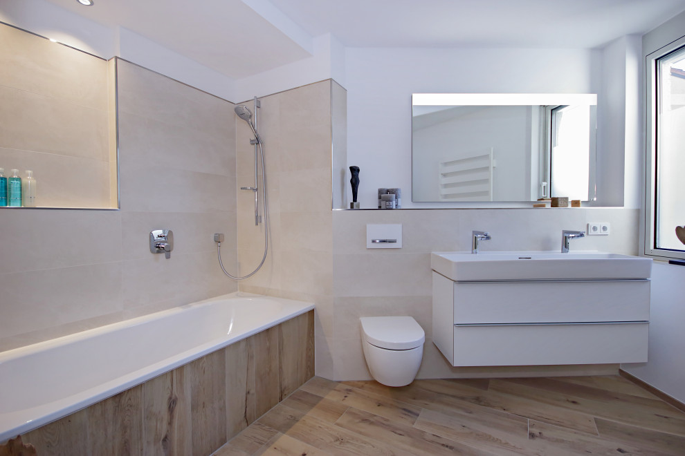 Idee per una grande stanza da bagno minimal con ante bianche, vasca da incasso, vasca/doccia, WC sospeso, piastrelle beige, pareti bianche, lavabo sospeso e pavimento marrone