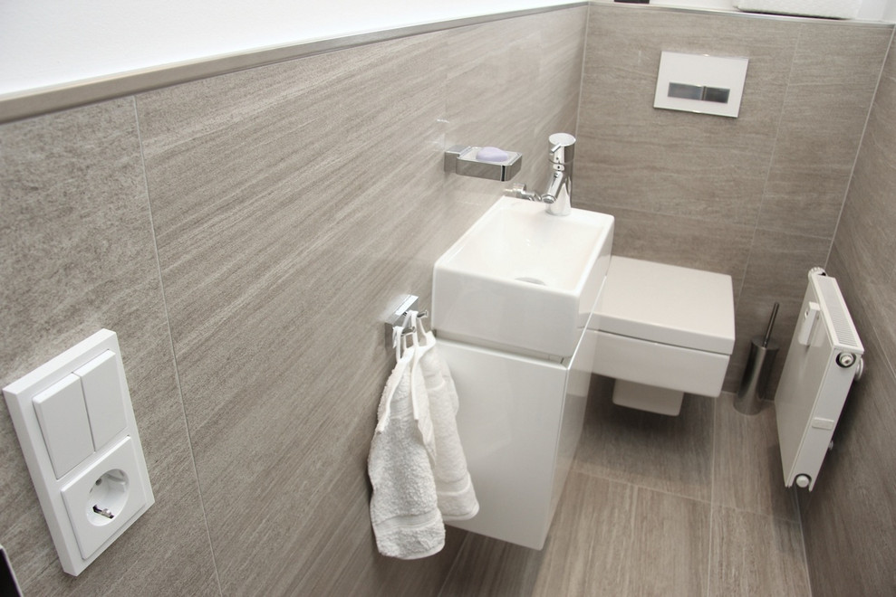 Kleines Modernes Badezimmer mit flächenbündigen Schrankfronten, weißen Schränken, Wandtoilette, beigen Fliesen, weißer Wandfarbe, Wandwaschbecken und beigem Boden in München