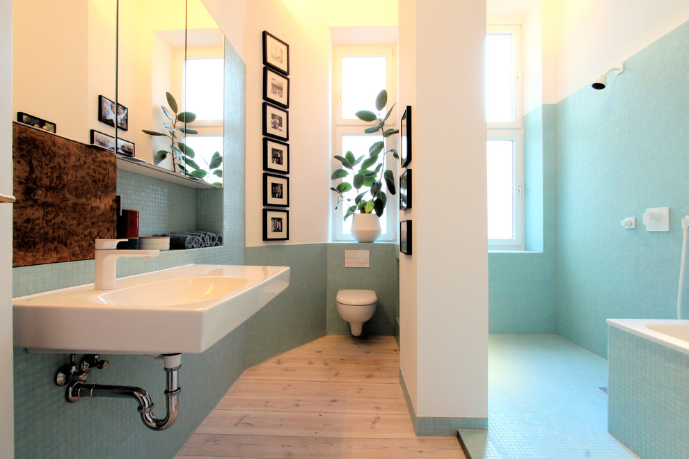 ベルリンにある広いコンテンポラリースタイルのおしゃれな浴室 (壁付け型シンク、バリアフリー、壁掛け式トイレ、青いタイル、モザイクタイル、白い壁、無垢フローリング、ドロップイン型浴槽) の写真