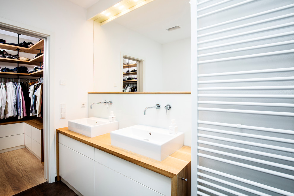 Idéer för att renovera ett mellanstort funkis en-suite badrum, med vita väggar, släta luckor, vita skåp, ett platsbyggt badkar, en kantlös dusch, en vägghängd toalettstol, vit kakel, porslinskakel, cementgolv, ett fristående handfat, träbänkskiva, brunt golv och med dusch som är öppen