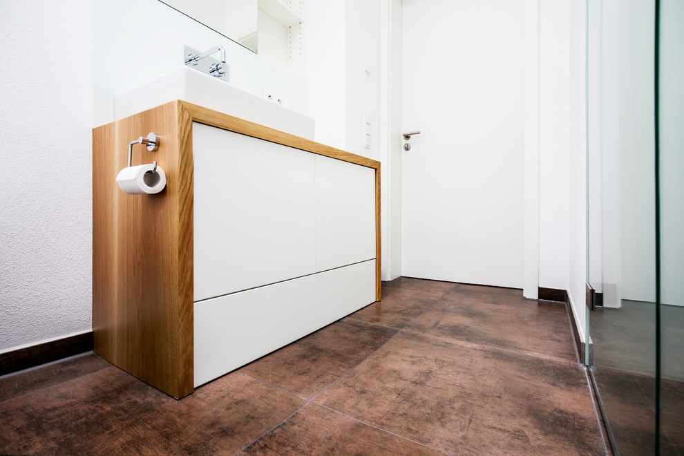 Example of a mid-sized trendy master white tile and porcelain tile cement tile floor and brown floor bathroom design in Munich with a wall-mount toilet, white walls, flat-panel cabinets, white cabinets, a vessel sink and wood countertops