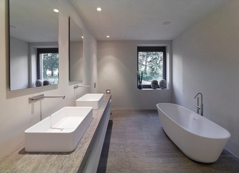 Modelo de cuarto de baño rectangular minimalista grande con lavabo sobreencimera, bañera exenta, paredes grises, losas de piedra, encimera de piedra caliza y suelo de piedra caliza