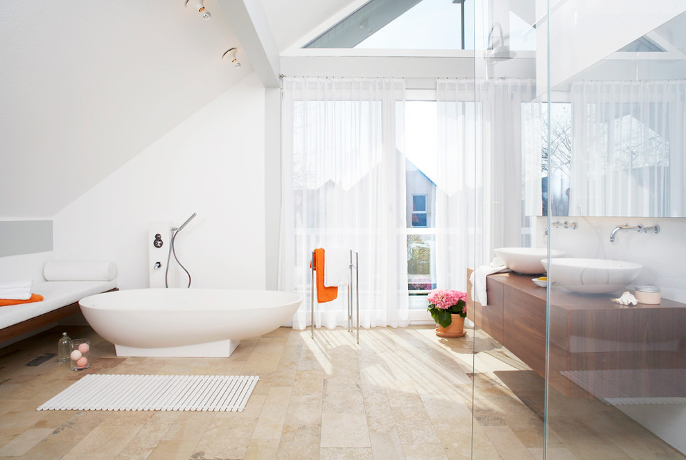 Foto på ett stort funkis badrum, med ett fristående handfat, ett fristående badkar, vita väggar, släta luckor, skåp i mellenmörkt trä, travertin golv och träbänkskiva
