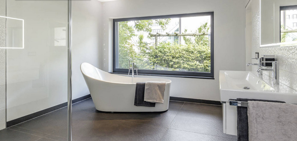 Cette image montre une grande salle de bain design avec une baignoire indépendante, une douche à l'italienne, un carrelage blanc, des carreaux de céramique, un mur blanc, un sol en ardoise, un lavabo suspendu et une fenêtre.