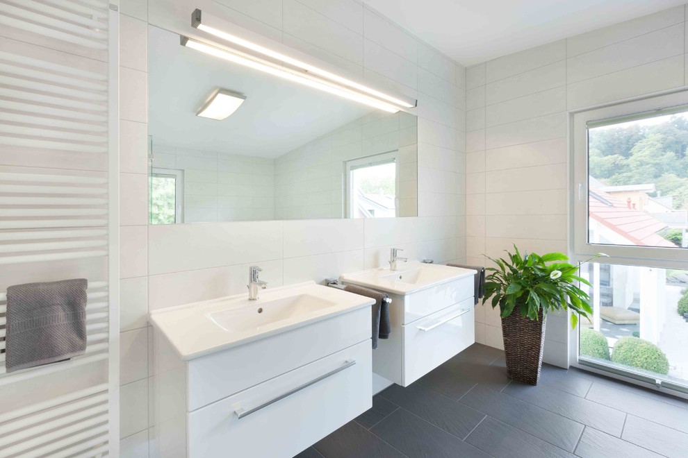 This is an example of an expansive contemporary shower room bathroom in Stuttgart with flat-panel cabinets, white cabinets, a built-in bath, a built-in shower, a two-piece toilet, white tiles, ceramic tiles, white walls, ceramic flooring, a submerged sink, solid surface worktops, black floors, an open shower and white worktops.
