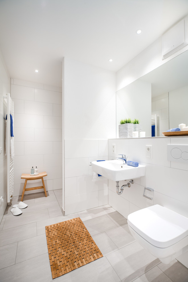 Exempel på ett litet modernt badrum med dusch, med en kantlös dusch, en vägghängd toalettstol, vit kakel, vita väggar, ett väggmonterat handfat, grått golv, med dusch som är öppen och porslinskakel