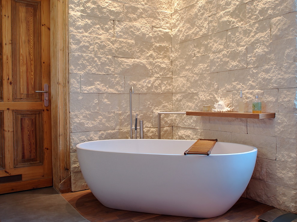 Idées déco pour une salle de bain beige et blanche contemporaine avec une baignoire indépendante, un carrelage de pierre, un mur beige et parquet foncé.