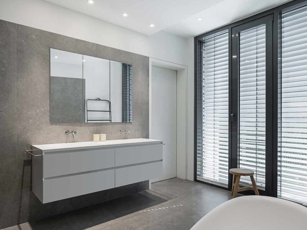 Diseño de cuarto de baño contemporáneo con bañera exenta, paredes grises, lavabo bajoencimera, encimera de acrílico, suelo gris y encimeras blancas