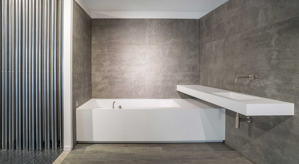 Cette photo montre une salle de bain tendance avec une baignoire posée, un mur gris, un plan de toilette en surface solide, un sol marron et un plan de toilette blanc.