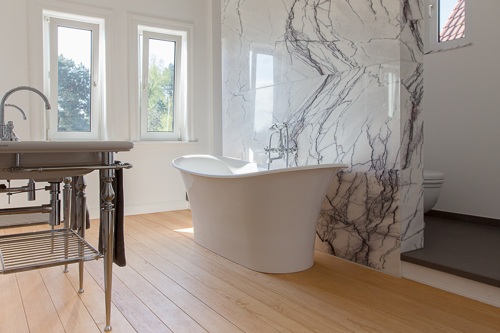 Foto på ett stort funkis badrum, med ett avlångt handfat, ett fristående badkar, stenkakel, vita väggar, mellanmörkt trägolv, svart kakel och vit kakel