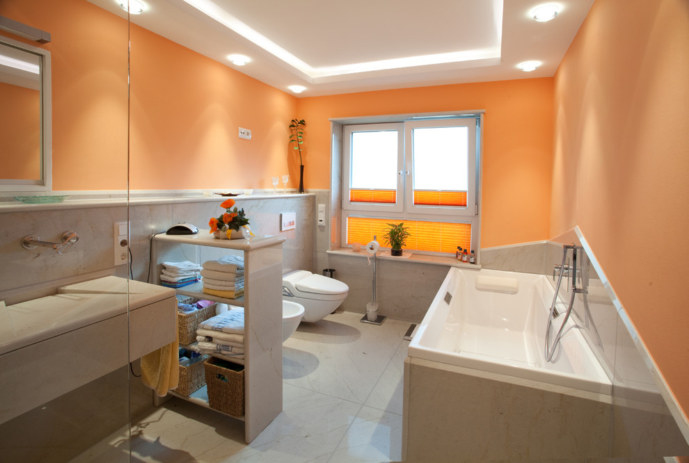 Immagine di una grande stanza da bagno con doccia minimal con ante lisce, ante beige, vasca da incasso, WC sospeso, piastrelle beige, piastrelle di marmo, pareti arancioni, pavimento in marmo, lavabo integrato, top in marmo e pavimento beige