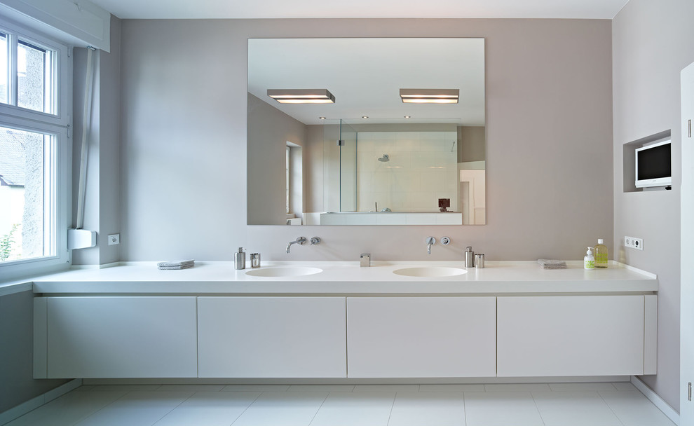 Großes Modernes Badezimmer mit integriertem Waschbecken, flächenbündigen Schrankfronten, weißen Schränken, weißen Fliesen, beiger Wandfarbe, Porzellan-Bodenfliesen und Mineralwerkstoff-Waschtisch in Frankfurt am Main