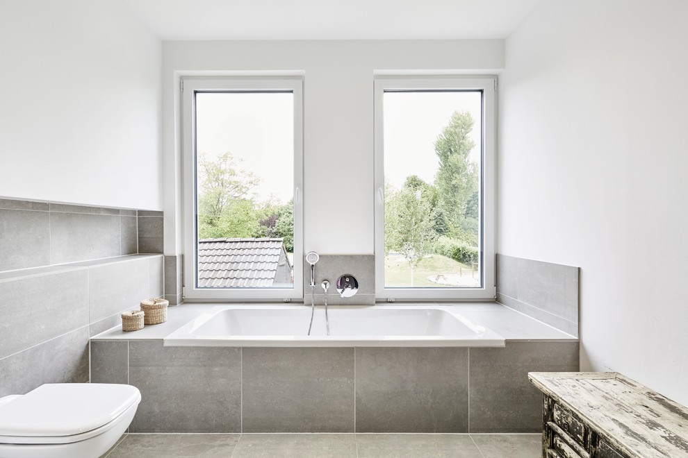 Modernes Badezimmer mit Badewanne in Nische, Wandtoilette, grauen Fliesen, weißer Wandfarbe, Keramikboden und grauem Boden in Essen