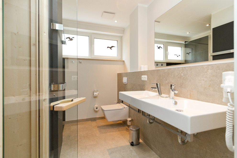 Imagen de cuarto de baño contemporáneo de tamaño medio con sanitario de pared, baldosas y/o azulejos beige, paredes blancas, suelo de travertino y lavabo suspendido
