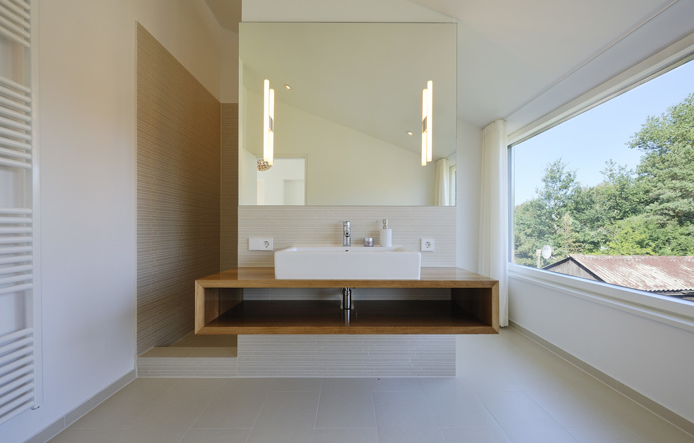 На фото: большая ванная комната в стиле модернизм с настольной раковиной, открытыми фасадами, фасадами цвета дерева среднего тона, серой плиткой, удлиненной плиткой, белыми стенами и столешницей из дерева