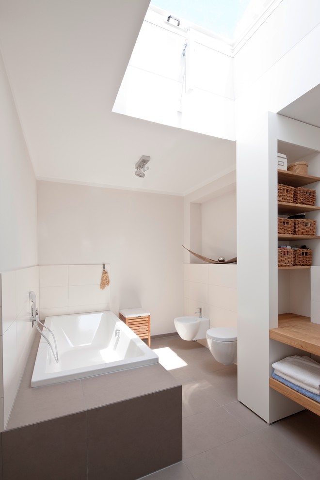 フランクフルトにある中くらいなコンテンポラリースタイルのおしゃれな浴室 (オープンシェルフ、ドロップイン型浴槽、壁掛け式トイレ、白いタイル、セラミックタイル、白い壁) の写真