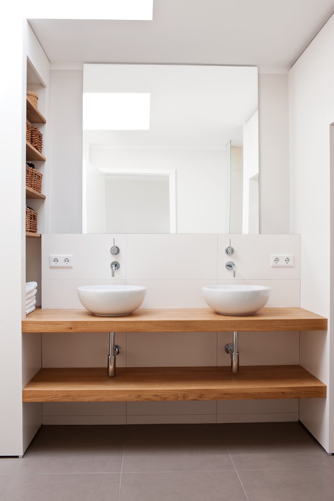 Modelo de cuarto de baño actual de tamaño medio con armarios abiertos, baldosas y/o azulejos blancos, baldosas y/o azulejos de cerámica, paredes blancas, lavabo sobreencimera y encimera de madera