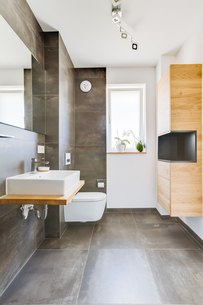 Modernes Badezimmer mit grauen Fliesen, weißer Wandfarbe, Aufsatzwaschbecken, Waschtisch aus Holz, grauem Boden, brauner Waschtischplatte und Einzelwaschbecken in Nürnberg