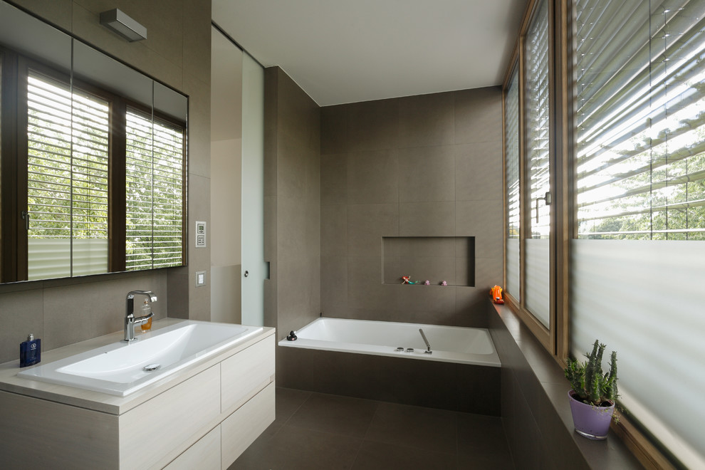 Modern inredning av ett stort badrum, med släta luckor, skåp i ljust trä, ett badkar i en alkov, brun kakel, bruna väggar, ett nedsänkt handfat och träbänkskiva
