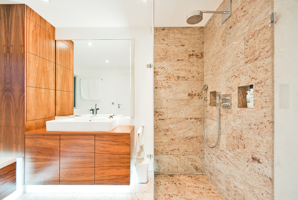 Cette image montre une salle d'eau design en bois brun de taille moyenne avec une vasque, un placard à porte plane, un plan de toilette en bois, une douche ouverte, un carrelage beige, un mur blanc, un carrelage de pierre, un sol en marbre et aucune cabine.