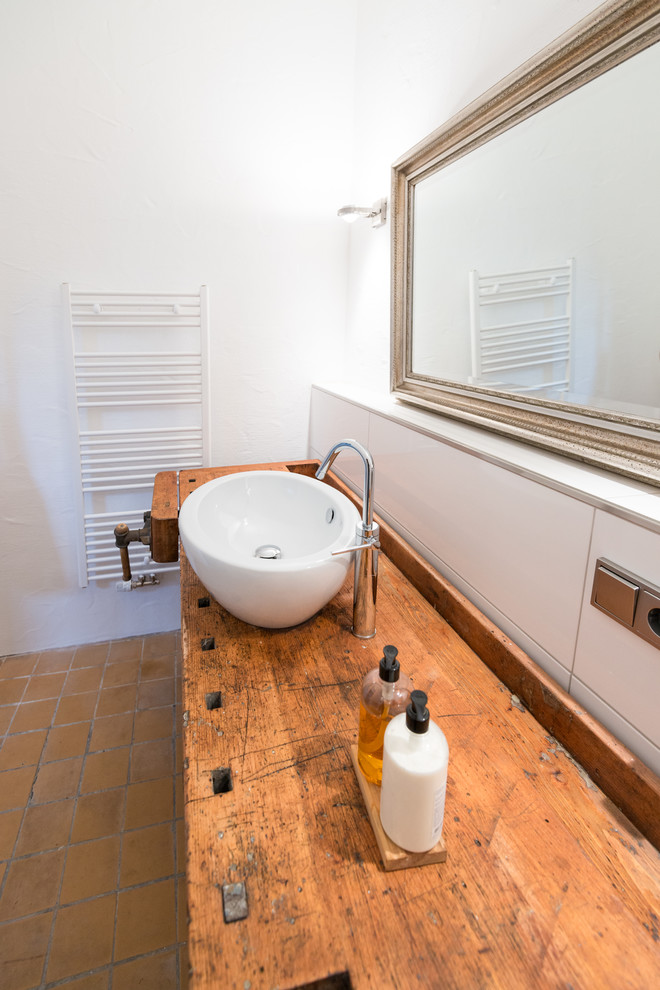 На фото: ванная комната среднего размера в современном стиле с белой плиткой, белыми стенами, полом из терракотовой плитки, настольной раковиной и столешницей из дерева