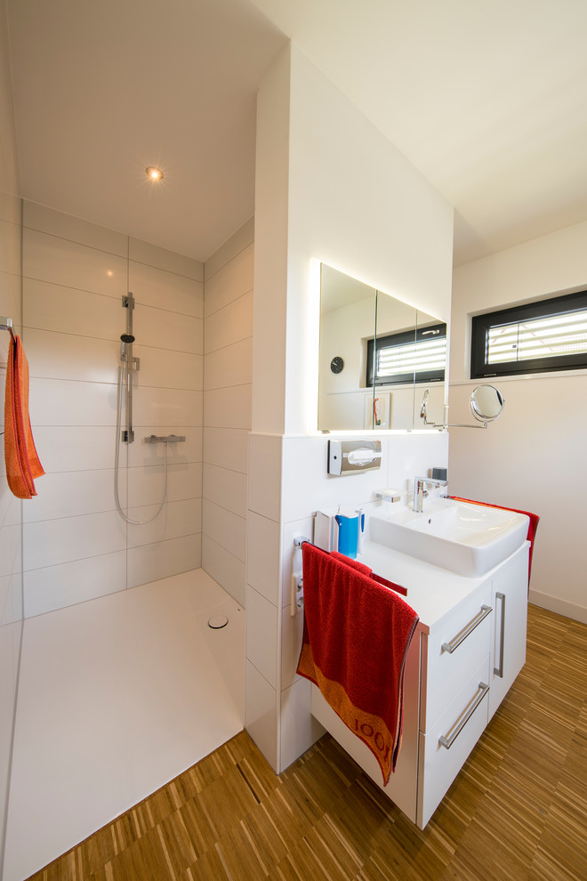 Modernes Badezimmer mit weißen Schränken, bodengleicher Dusche, weißen Fliesen, weißer Wandfarbe, hellem Holzboden, Aufsatzwaschbecken, braunem Boden, offener Dusche und weißer Waschtischplatte in Sonstige