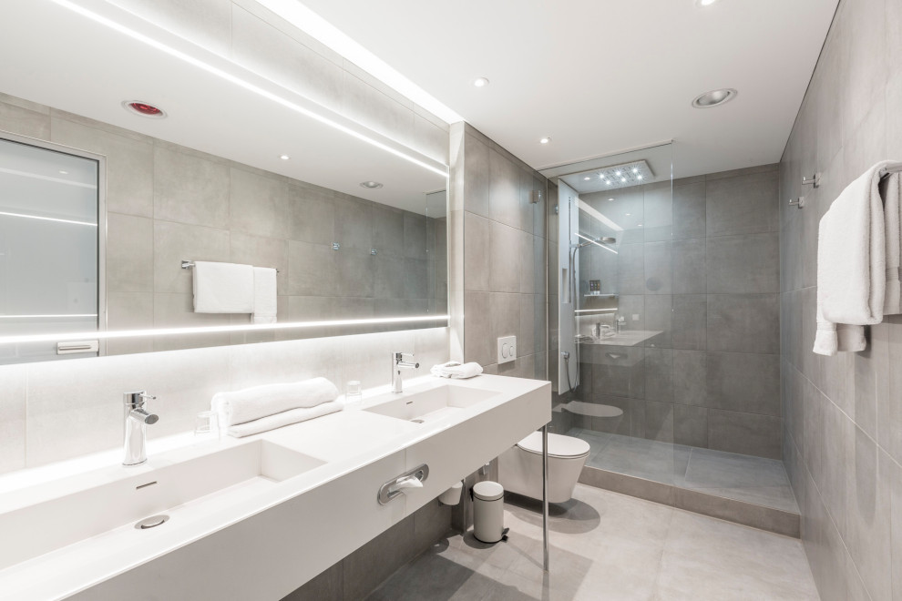 Modelo de cuarto de baño contemporáneo grande con ducha empotrada, sanitario de pared, baldosas y/o azulejos grises, baldosas y/o azulejos de porcelana, suelo de baldosas de porcelana, aseo y ducha, lavabo integrado, suelo gris y encimeras blancas