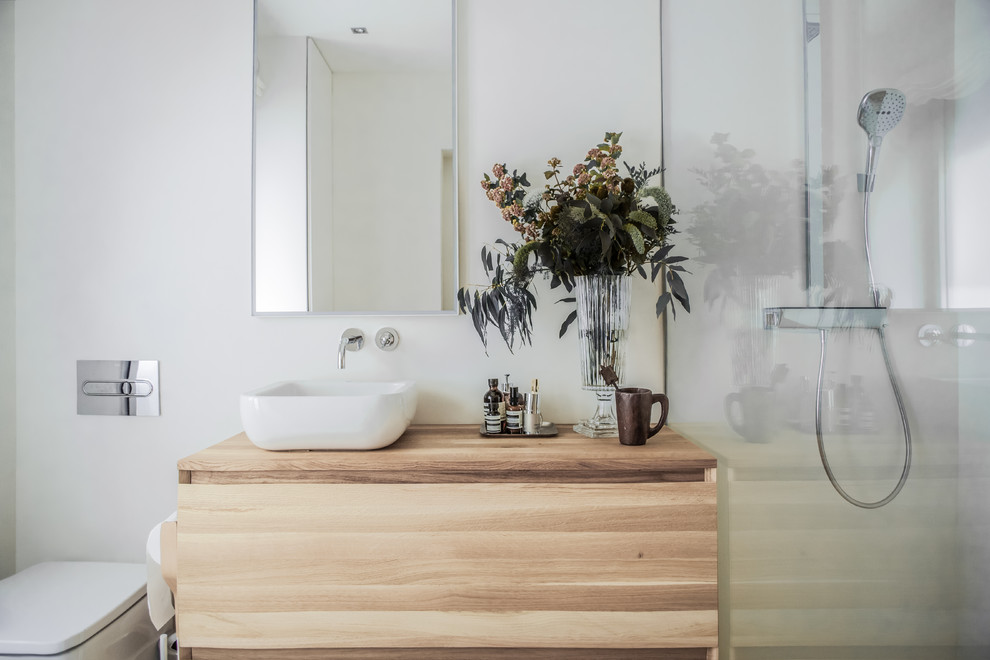 Inredning av ett modernt mellanstort beige beige badrum med dusch, med skåp i ljust trä, vit kakel, öppna hyllor, ett fristående badkar, en kantlös dusch, en vägghängd toalettstol, kakelplattor, bruna väggar, ljust trägolv, ett fristående handfat, träbänkskiva, brunt golv och med dusch som är öppen