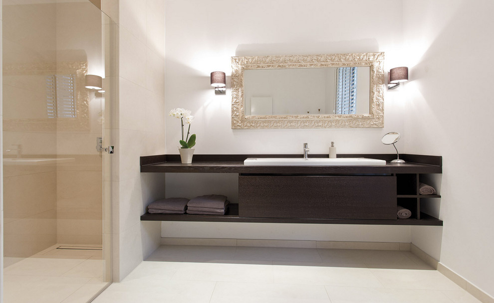На фото: ванная комната среднего размера в современном стиле с плоскими фасадами, темными деревянными фасадами, душем без бортиков, бежевой плиткой, белыми стенами, накладной раковиной, столешницей из дерева, каменной плиткой и душевой кабиной