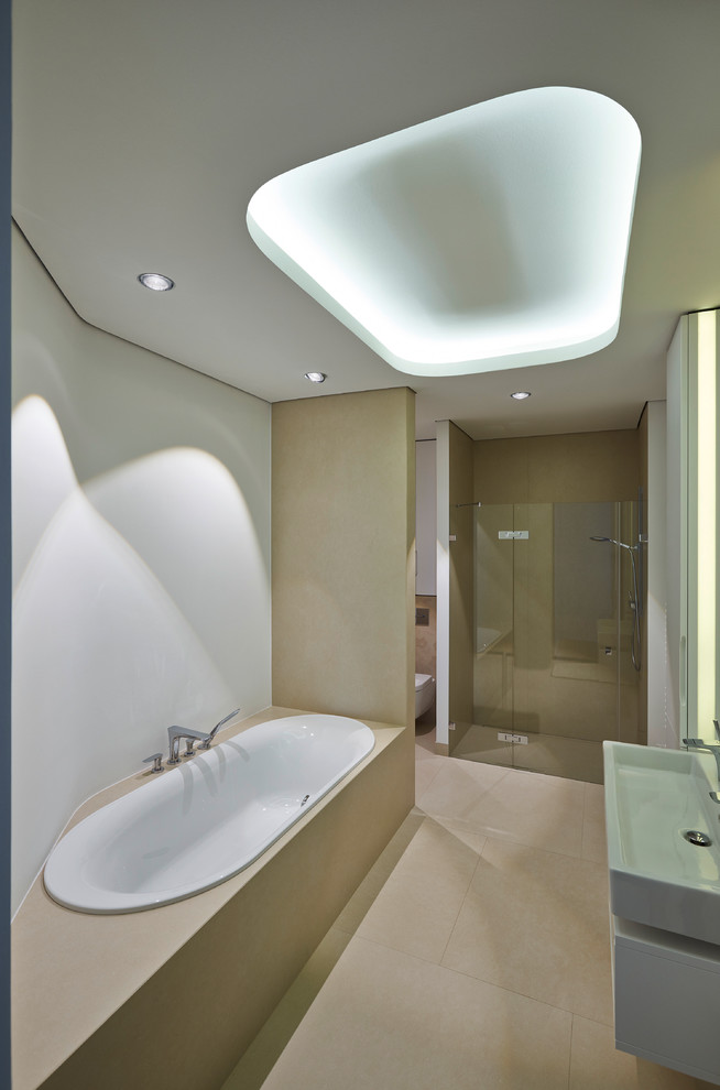 Medium sized contemporary bathroom in Munich with a built-in bath, an alcove shower, a wall mounted toilet, beige tiles, white walls, travertine flooring, a trough sink and a hinged door.