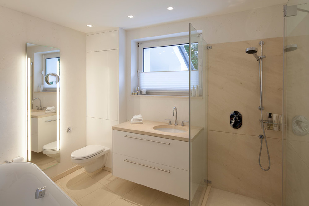 Inspiration for a small traditional ensuite wet room bathroom in Cologne with white cabinets, a wall mounted toilet, white walls, flat-panel cabinets, a built-in bath, travertine tiles, a built-in sink, limestone worktops and a hinged door.