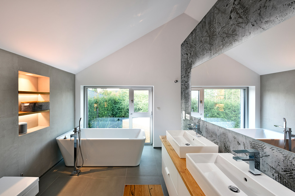 Inspiration for a medium sized contemporary shower room bathroom in Nuremberg with flat-panel cabinets, white cabinets, a freestanding bath, a wall mounted toilet, a vessel sink, wooden worktops, grey floors, grey walls, a shower/bath combination, cement flooring and an open shower.