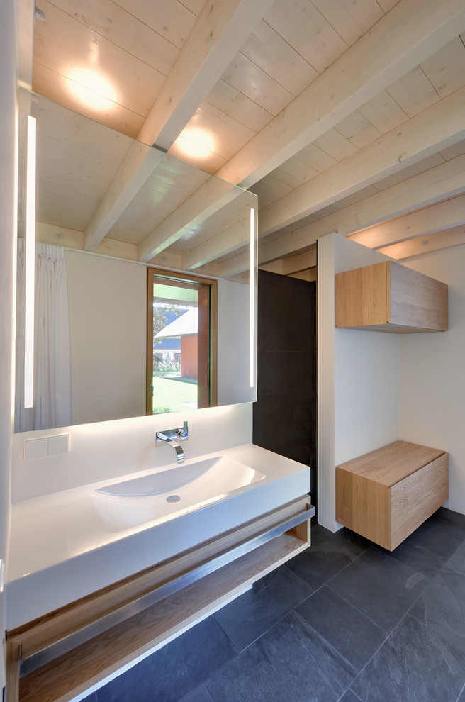Modelo de cuarto de baño contemporáneo con armarios con paneles lisos, puertas de armario de madera oscura, paredes blancas, suelo de pizarra y lavabo integrado