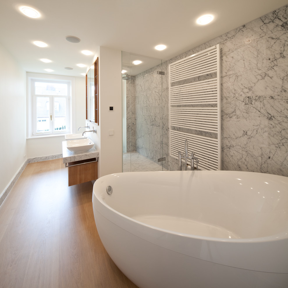 Réalisation d'une grande douche en alcôve design en bois brun avec une baignoire indépendante, un carrelage gris, des dalles de pierre, un mur blanc, un sol en bois brun, une vasque et un plan de toilette en marbre.