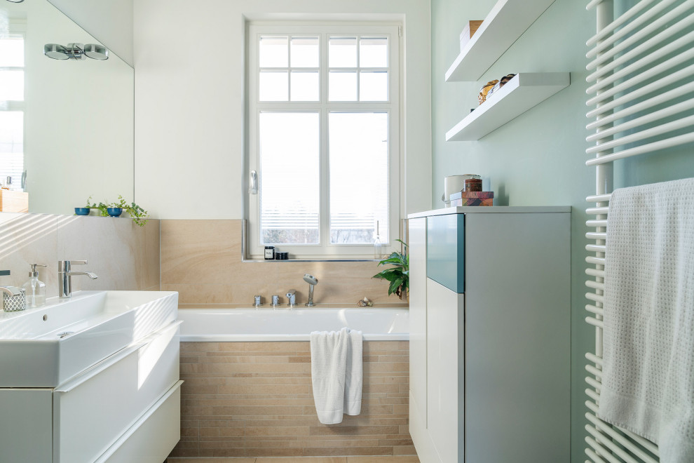Photo of a medium sized contemporary bathroom in Berlin with turquoise cabinets, a built-in bath, a wall mounted toilet, beige tiles and an integrated sink.