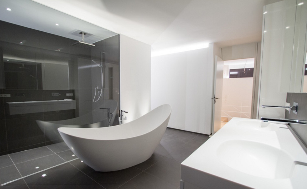 Geräumiges Modernes Badezimmer mit bodengleicher Dusche, grauen Fliesen, weißer Wandfarbe, integriertem Waschbecken und freistehender Badewanne in Stuttgart