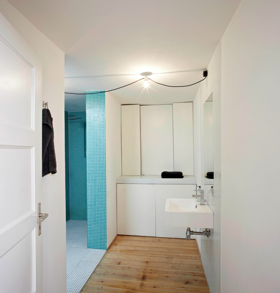 Idée de décoration pour une douche en alcôve design de taille moyenne avec un lavabo suspendu, un placard à porte plane, des portes de placard blanches, un carrelage bleu, un carrelage blanc, mosaïque, un mur blanc et un sol en bois brun.