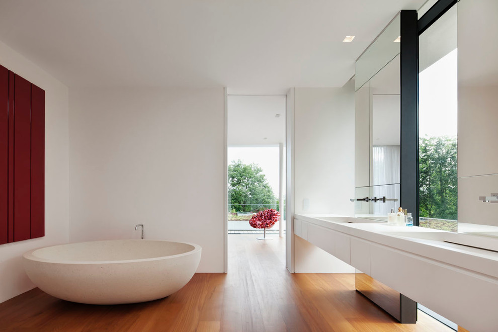Inspiration pour une salle de bain design avec un placard à porte plane, des portes de placard blanches, un mur blanc, un sol en bois brun, un lavabo intégré et une baignoire indépendante.