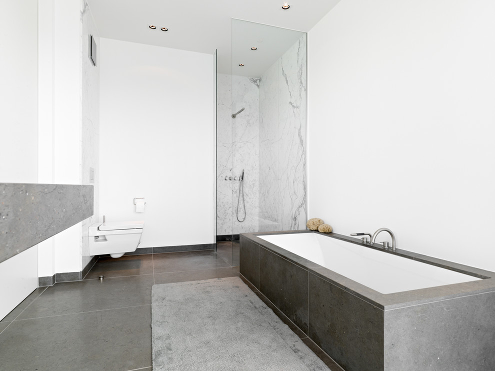 Bild på ett litet funkis badrum, med ett badkar i en alkov, en vägghängd toalettstol, vita väggar, en öppen dusch, grå kakel och med dusch som är öppen