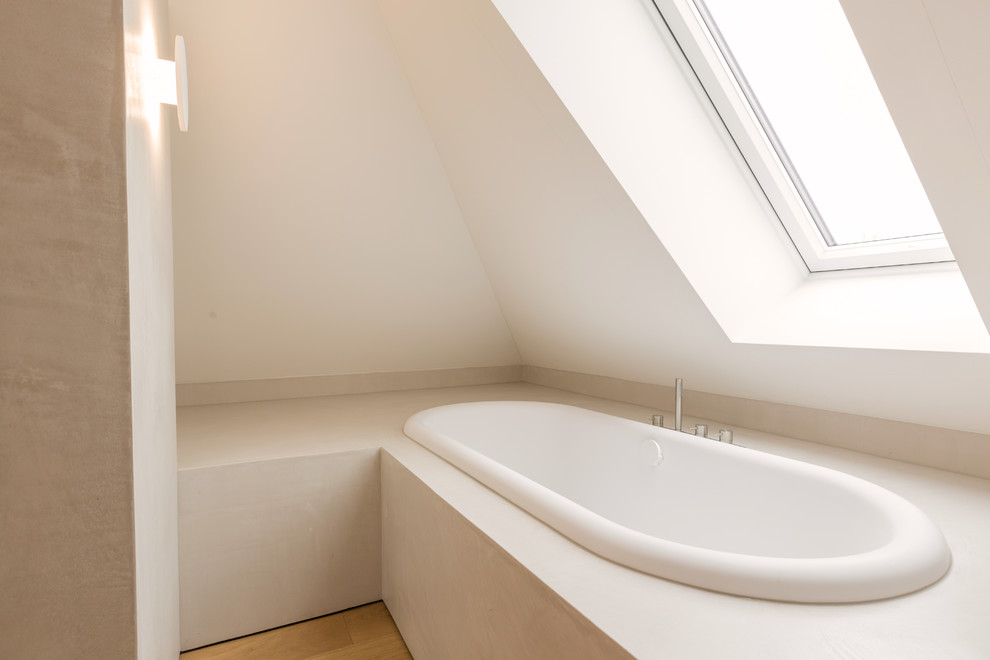 Example of a large minimalist master beige tile and travertine tile light wood floor and beige floor drop-in bathtub design in Munich with flat-panel cabinets, white cabinets, a wall-mount toilet, white walls, a vessel sink and solid surface countertops