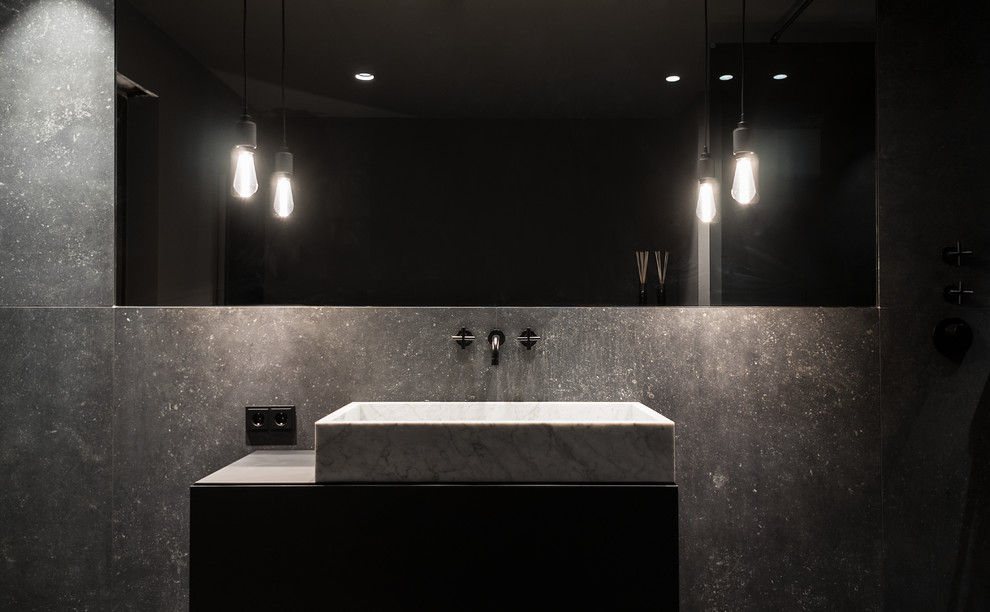 Inredning av ett modernt mellanstort svart svart en-suite badrum, med släta luckor, svarta skåp, ett fristående badkar, en kantlös dusch, en vägghängd toalettstol, svart kakel, keramikplattor, svarta väggar, klinkergolv i keramik, ett fristående handfat, bänkskiva i akrylsten, svart golv och med dusch som är öppen