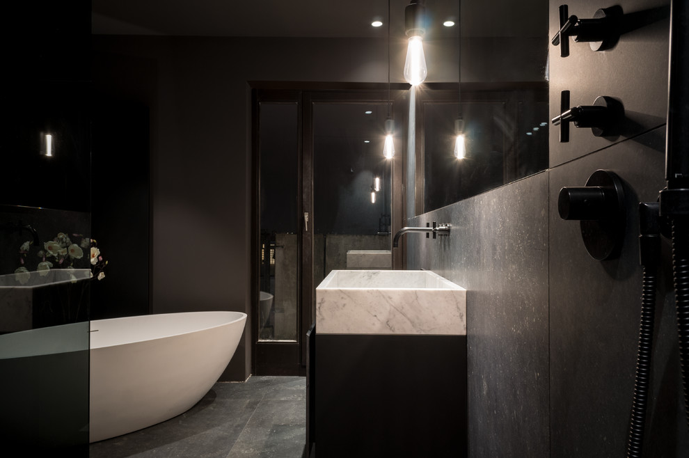 Inspiration för mellanstora moderna svart en-suite badrum, med släta luckor, svarta skåp, ett fristående badkar, en kantlös dusch, en vägghängd toalettstol, svart kakel, keramikplattor, svarta väggar, klinkergolv i keramik, ett fristående handfat, bänkskiva i akrylsten, svart golv och med dusch som är öppen