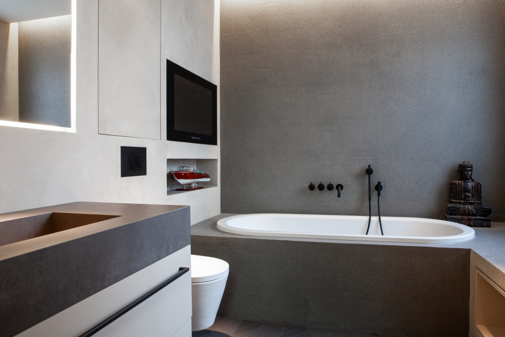 Inspiration för ett stort industriellt svart svart en-suite badrum, med släta luckor, skåp i mörkt trä, ett undermonterat badkar, en kantlös dusch, en vägghängd toalettstol, stickkakel, grå väggar, mosaikgolv, ett integrerad handfat, granitbänkskiva, grått golv och med dusch som är öppen