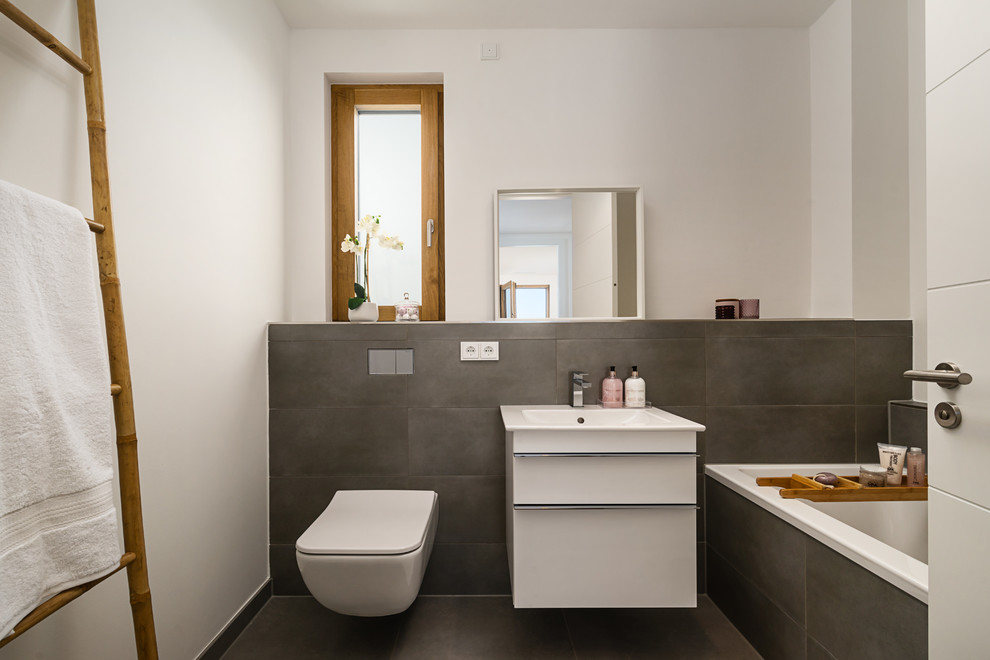 Aménagement d'une petite salle d'eau contemporaine avec un placard à porte plane, des portes de placard blanches, une baignoire posée, WC suspendus, un carrelage gris, des carreaux de béton, un mur blanc, un plan vasque et un sol gris.