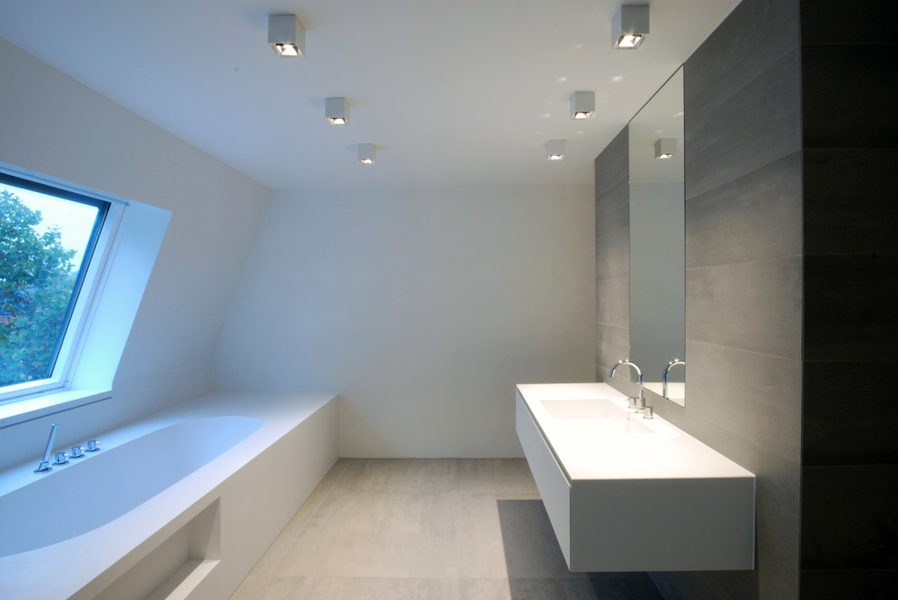 This is an example of a medium sized modern shower room bathroom in Cologne with grey tiles, ceramic tiles, solid surface worktops, flat-panel cabinets, white cabinets, a built-in bath, white walls, cement flooring, an integrated sink, beige floors and white worktops.