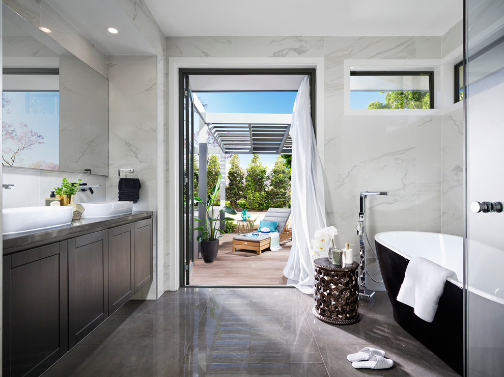 Cette photo montre une grande salle de bain tendance avec un placard à porte shaker, des portes de placard noires, une baignoire indépendante, un carrelage blanc, des dalles de pierre, un mur blanc et une vasque.