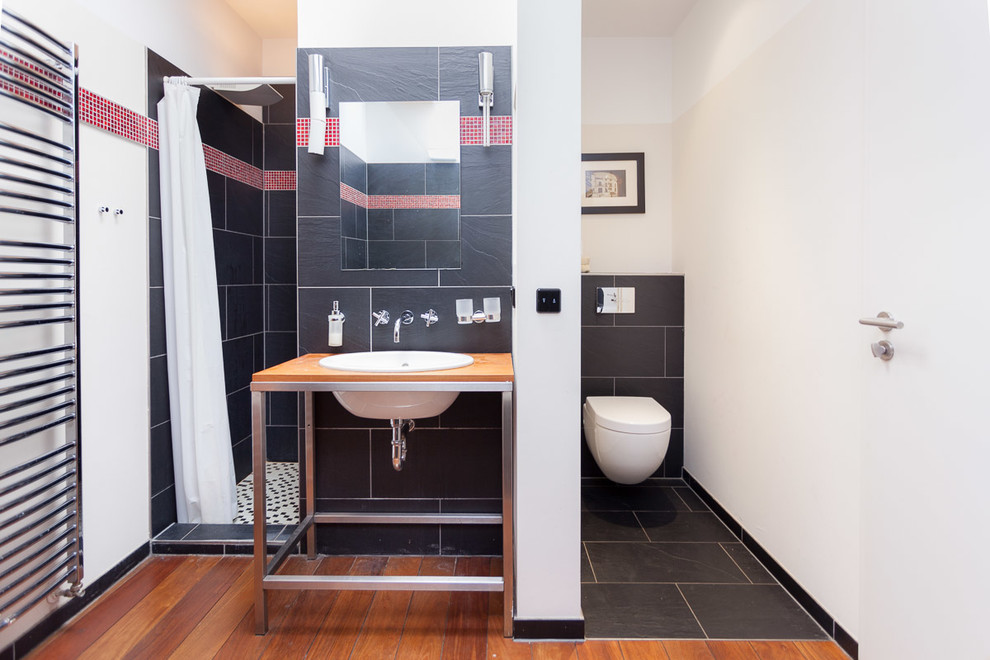 Kleines Modernes Duschbad mit Einbauwaschbecken, Waschtisch aus Holz, schwarzen Fliesen, weißer Wandfarbe, Duschnische, Wandtoilette, Steinfliesen und braunem Holzboden in Sonstige