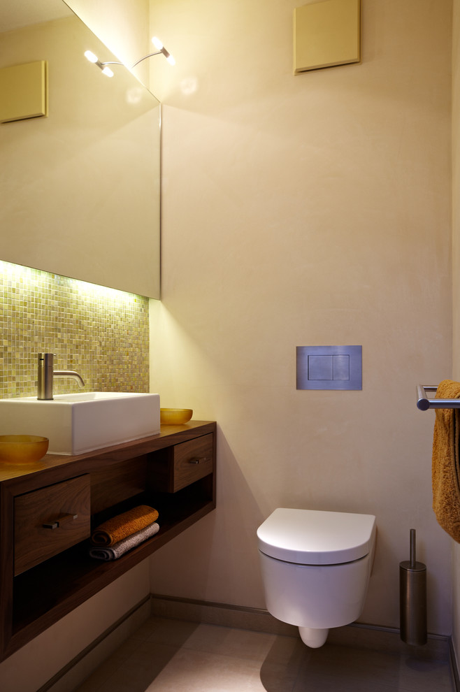 Aménagement d'une salle de bain contemporaine en bois foncé avec WC suspendus, mosaïque, un mur beige, une vasque, un plan de toilette en bois, un placard sans porte, un carrelage vert et un plan de toilette marron.