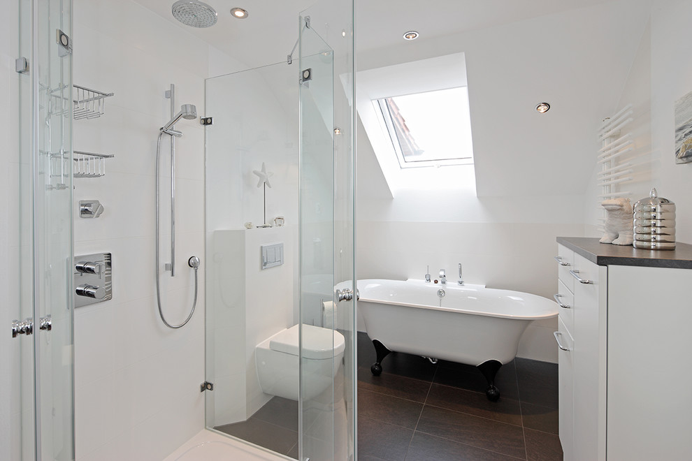 Ejemplo de cuarto de baño actual pequeño con armarios con paneles lisos, bañera exenta, sanitario de pared, baldosas y/o azulejos grises, paredes blancas y puertas de armario blancas
